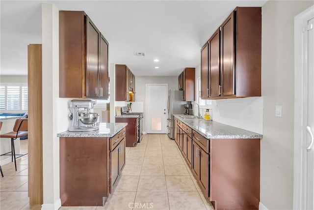 kitchen with light stone counters, light tile patterned floors, appliances with stainless steel finishes, and sink