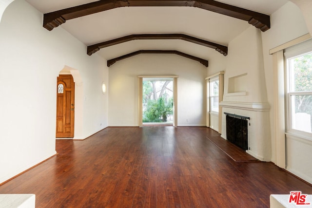 unfurnished living room featuring dark wood-type flooring, a tiled fireplace, lofted ceiling with beams, and a wealth of natural light