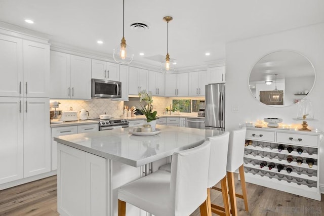 kitchen with pendant lighting, white cabinetry, a center island, stainless steel appliances, and light stone countertops