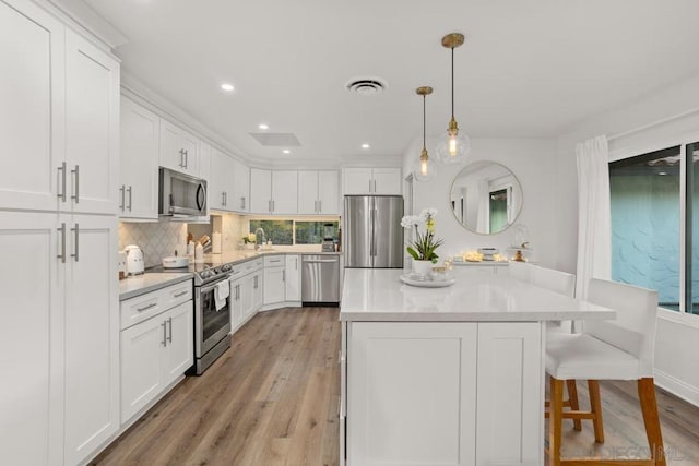 kitchen with white cabinets, pendant lighting, stainless steel appliances, light hardwood / wood-style floors, and backsplash