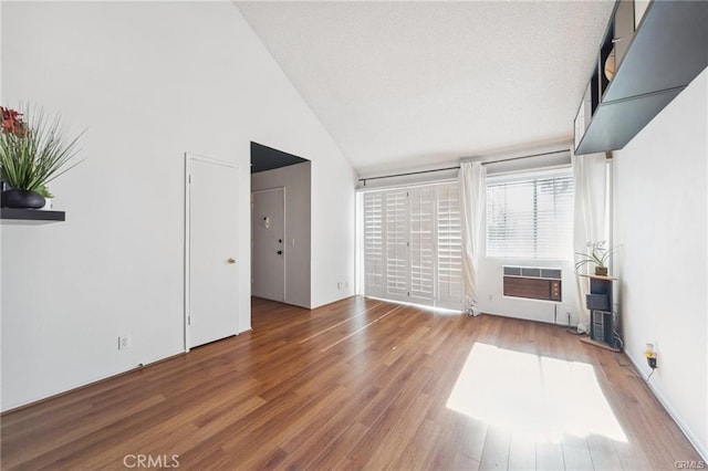 unfurnished living room with an AC wall unit, hardwood / wood-style flooring, and high vaulted ceiling