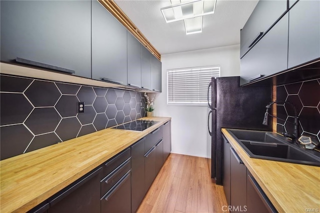 kitchen featuring backsplash, sink, black electric stovetop, and light hardwood / wood-style flooring