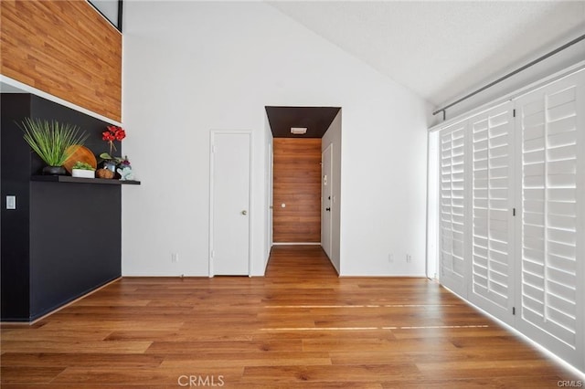 unfurnished bedroom with light hardwood / wood-style floors, lofted ceiling, and wooden walls