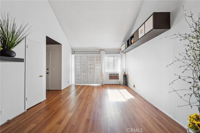 unfurnished living room with hardwood / wood-style flooring, a wall unit AC, and lofted ceiling