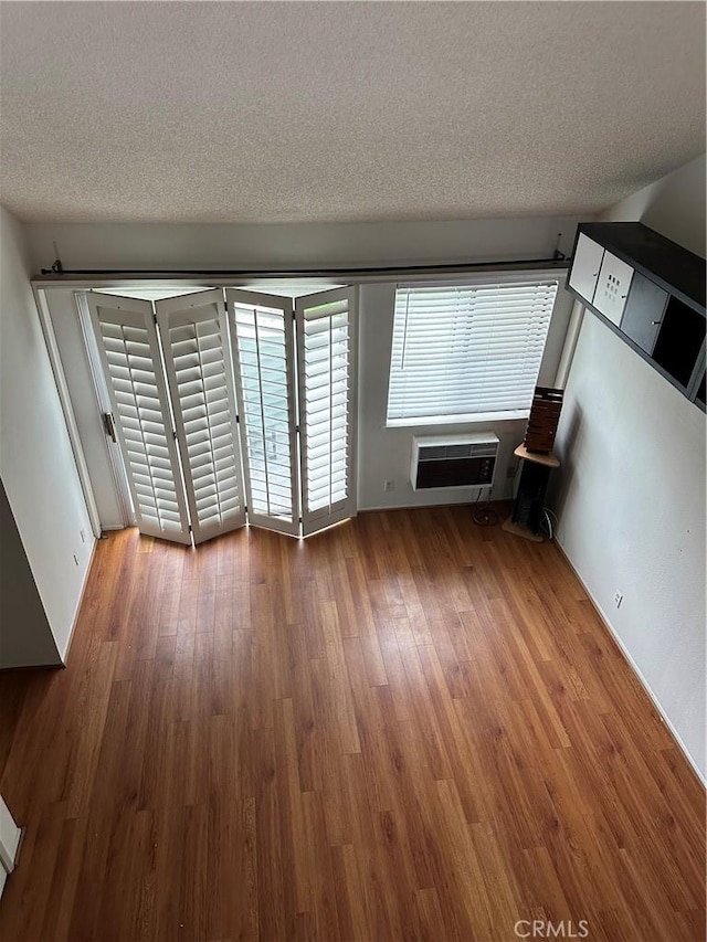 unfurnished living room featuring a textured ceiling, hardwood / wood-style flooring, and a wall mounted air conditioner