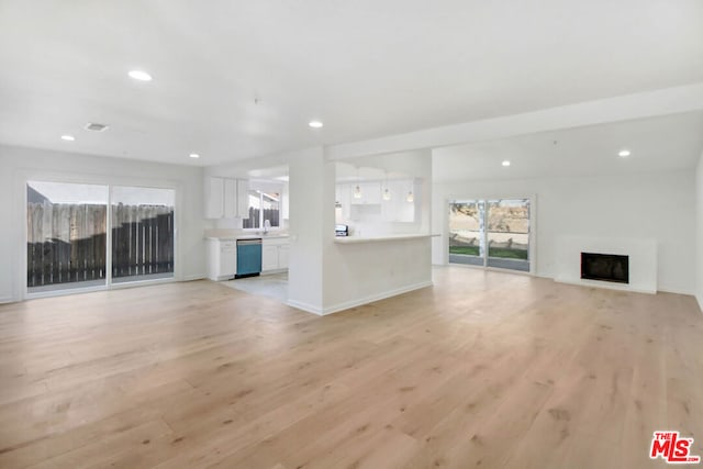 unfurnished living room with sink, light wood-type flooring, and a wealth of natural light