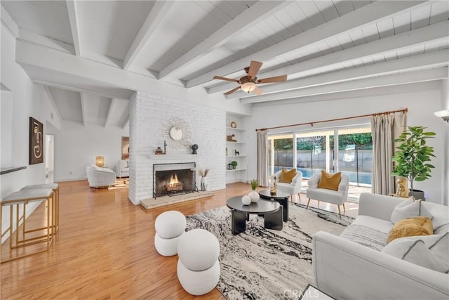 living room with wood-type flooring, beamed ceiling, a fireplace, built in features, and ceiling fan