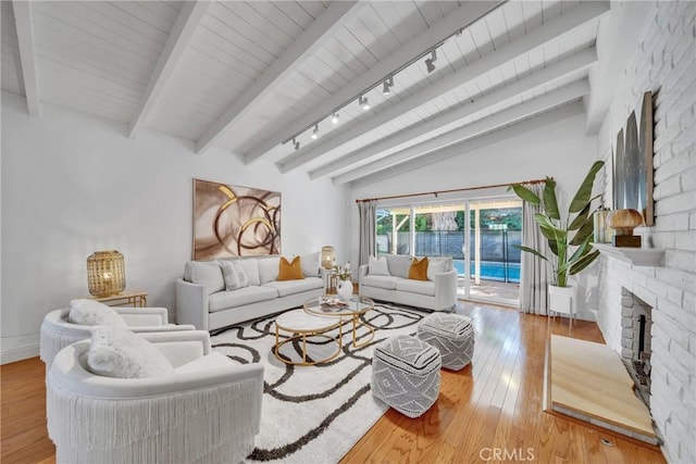 living room with a brick fireplace, rail lighting, wood-type flooring, and vaulted ceiling with beams