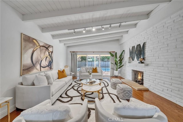 living room with track lighting, a fireplace, hardwood / wood-style flooring, and lofted ceiling with beams