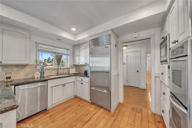 kitchen featuring decorative backsplash, sink, built in appliances, light wood-type flooring, and white cabinets