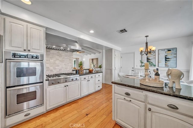 kitchen with stainless steel appliances, wall chimney exhaust hood, light hardwood / wood-style flooring, and white cabinetry