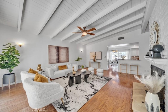 living room featuring ceiling fan with notable chandelier, a large fireplace, light hardwood / wood-style floors, and lofted ceiling with beams