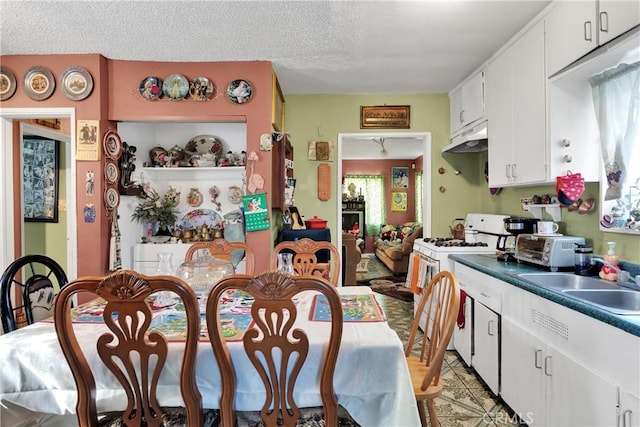 kitchen featuring a textured ceiling, white cabinets, white range with gas stovetop, and sink