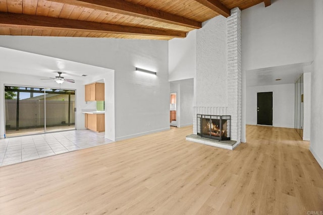 unfurnished living room with light hardwood / wood-style floors, ceiling fan, a brick fireplace, wooden ceiling, and beam ceiling