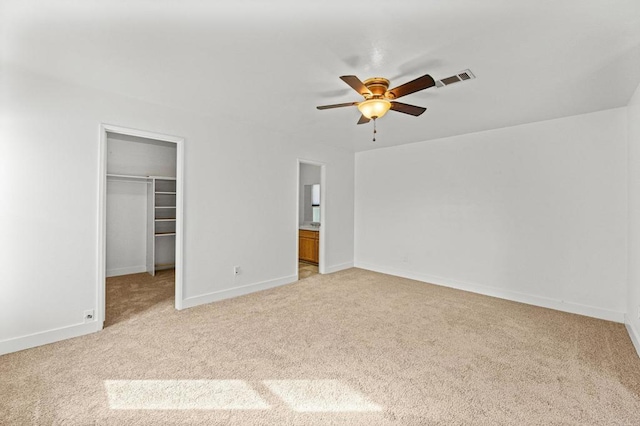 unfurnished bedroom featuring ceiling fan, ensuite bathroom, a spacious closet, light carpet, and a closet