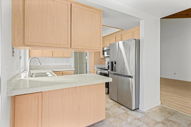 kitchen featuring kitchen peninsula, appliances with stainless steel finishes, tile counters, light brown cabinetry, and sink