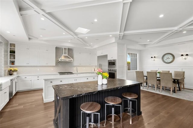 kitchen with wall chimney exhaust hood, coffered ceiling, a breakfast bar, a large island, and white cabinets