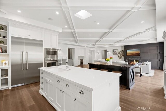 kitchen featuring a spacious island, white cabinets, built in appliances, and coffered ceiling