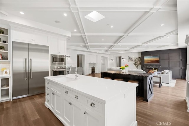 kitchen featuring coffered ceiling, white cabinetry, a large island, and built in appliances