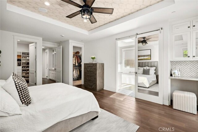 bedroom featuring ensuite bathroom, ceiling fan, dark hardwood / wood-style floors, a tray ceiling, and a walk in closet