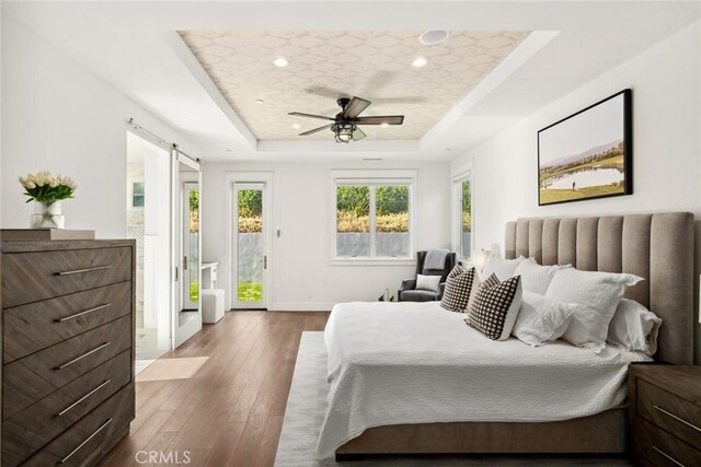 bedroom featuring ceiling fan, a barn door, access to exterior, and a tray ceiling