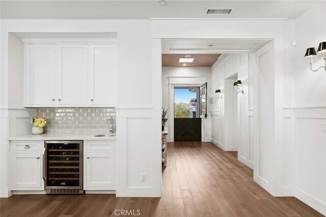 bar featuring white cabinetry, hardwood / wood-style flooring, decorative backsplash, beverage cooler, and sink