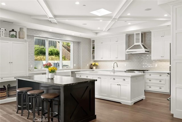 kitchen featuring wall chimney range hood, white cabinets, and an island with sink