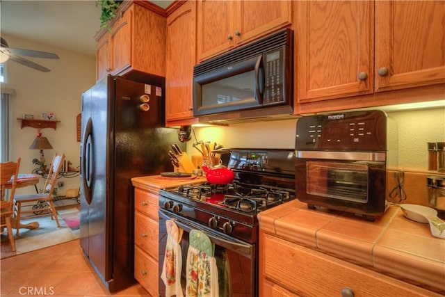 kitchen featuring light tile patterned flooring, ceiling fan, tile counters, and black appliances