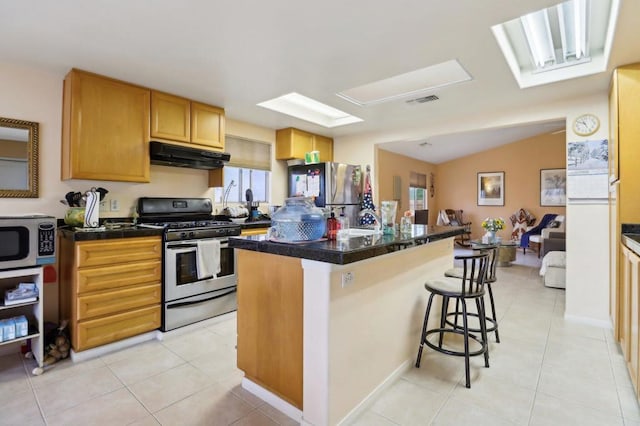 kitchen with vaulted ceiling, a center island with sink, a breakfast bar, light tile patterned flooring, and appliances with stainless steel finishes