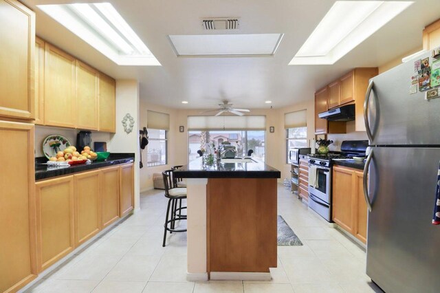 kitchen featuring a kitchen island, a skylight, stainless steel appliances, a kitchen breakfast bar, and ceiling fan