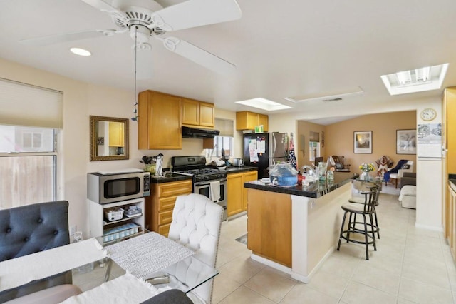 kitchen with light tile patterned floors, a kitchen bar, ceiling fan, stainless steel appliances, and a kitchen island