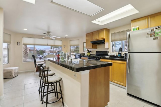 kitchen featuring stainless steel fridge, an island with sink, ceiling fan, black range, and a breakfast bar