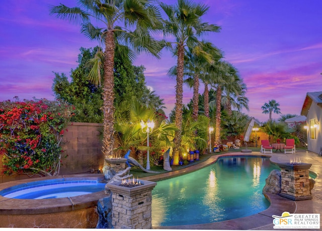 pool at dusk with an in ground hot tub and a patio