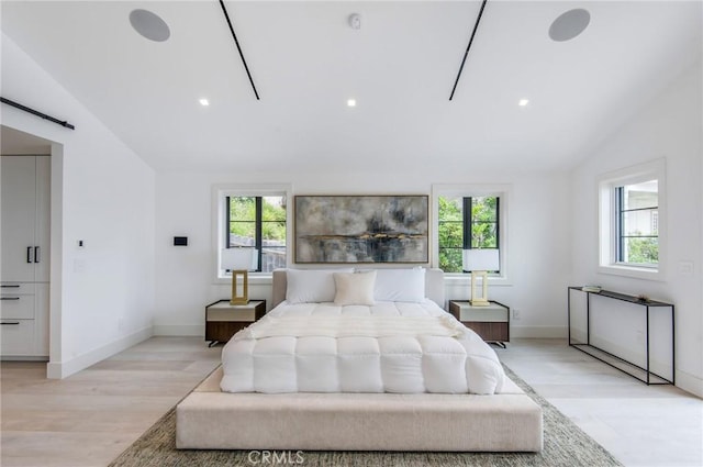 bedroom with a barn door, vaulted ceiling, multiple windows, and light hardwood / wood-style floors