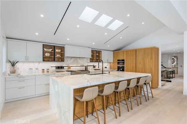 kitchen with a large island, backsplash, white cabinets, lofted ceiling with skylight, and light stone counters