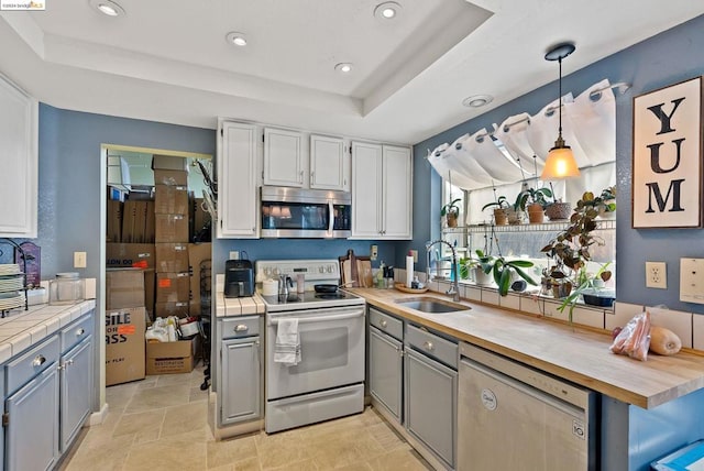 kitchen with pendant lighting, butcher block countertops, sink, a tray ceiling, and stainless steel appliances