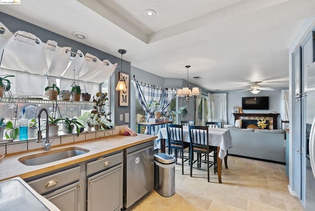 kitchen featuring pendant lighting, sink, gray cabinetry, ceiling fan with notable chandelier, and stainless steel dishwasher