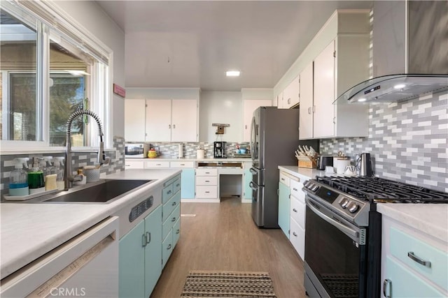 kitchen featuring wall chimney exhaust hood, appliances with stainless steel finishes, light countertops, white cabinetry, and a sink