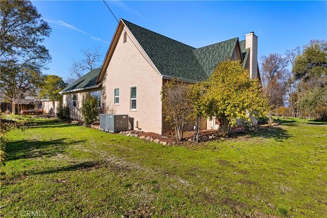 view of property exterior featuring roof with shingles, a yard, a chimney, stucco siding, and central air condition unit