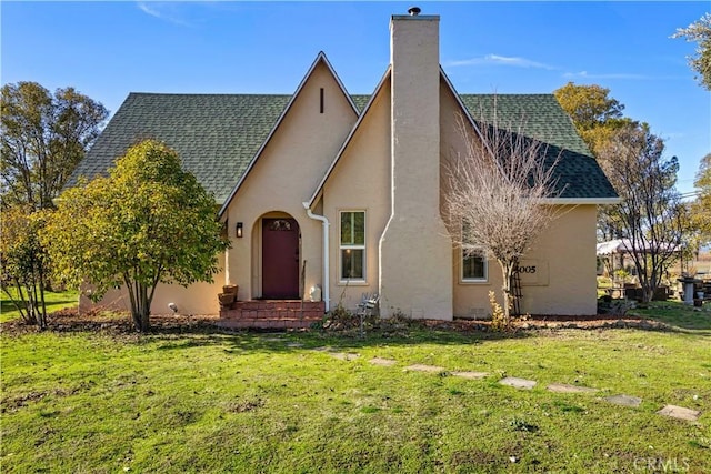 view of front facade featuring a shingled roof, a front yard, a chimney, and stucco siding