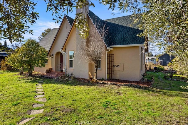 back of house with stucco siding, roof with shingles, and a yard