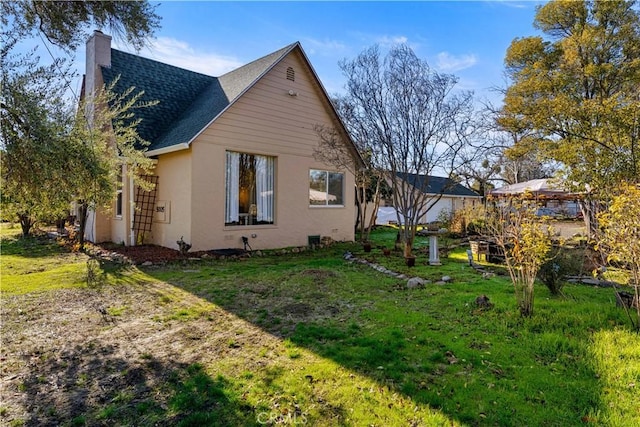 view of side of home featuring a shingled roof, a lawn, a chimney, and stucco siding