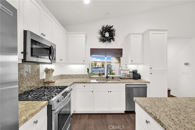 kitchen featuring lofted ceiling, sink, white cabinetry, stainless steel appliances, and light stone counters