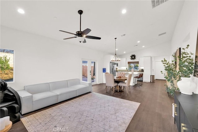 living room with dark hardwood / wood-style flooring, ceiling fan with notable chandelier, and high vaulted ceiling