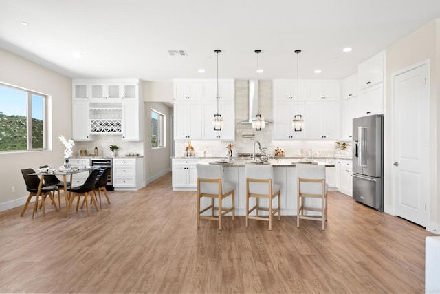 kitchen featuring high quality fridge, white cabinetry, hanging light fixtures, a kitchen island with sink, and light wood-type flooring