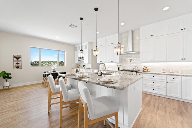 kitchen with light stone countertops, white cabinetry, sink, and wall chimney range hood