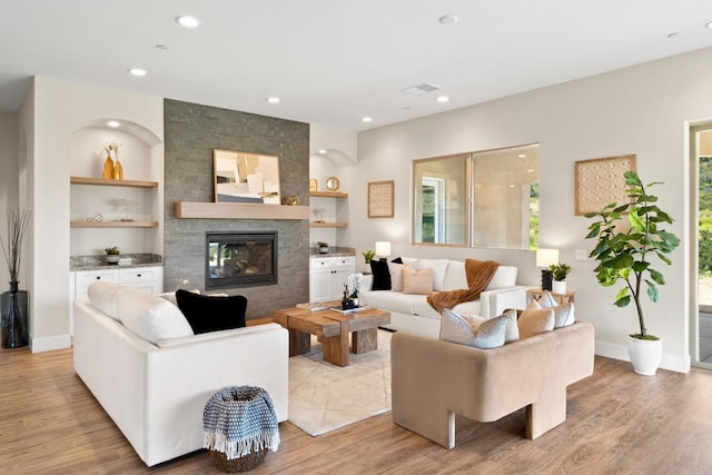 living room with built in features, a large fireplace, plenty of natural light, and light hardwood / wood-style floors