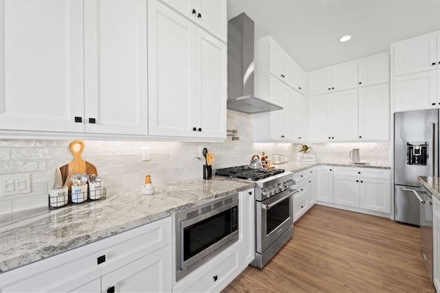 kitchen featuring premium appliances, white cabinetry, wall chimney range hood, light hardwood / wood-style floors, and backsplash