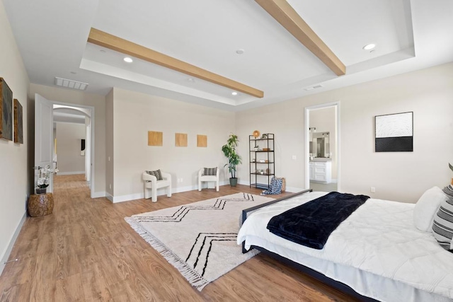 bedroom featuring ensuite bathroom, light wood-type flooring, and a raised ceiling