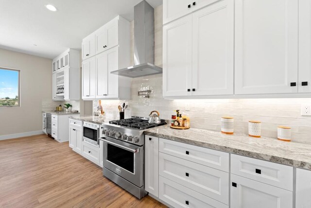 kitchen with light stone countertops, white cabinetry, wall chimney range hood, stainless steel appliances, and light hardwood / wood-style flooring